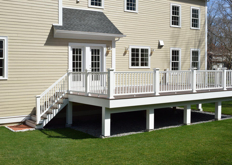 best decking material-deck with white railing off a tan sided house